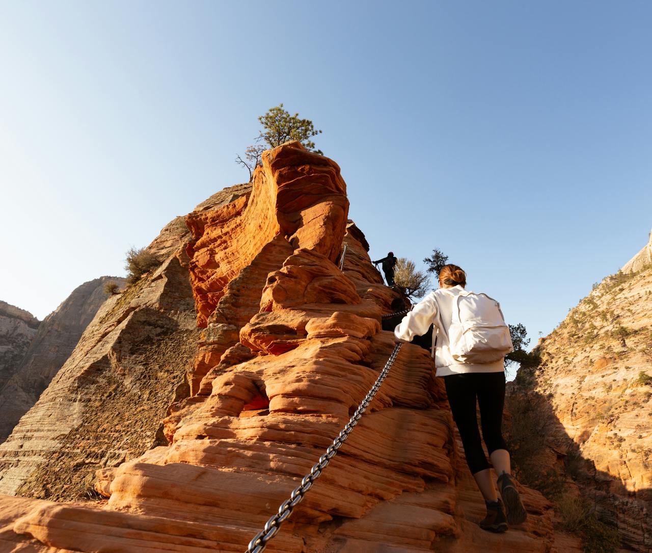 Hiker climbs rocky terrain in Zion National Park, showcasing the dramatic sandstone cliffs.